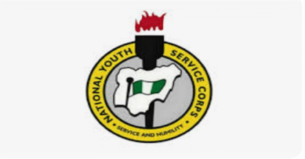 Nigerian NYSC corps members in white uniforms checking mobile phones for allowance payment alerts after receiving overdue ₦77,000 monthly stipends